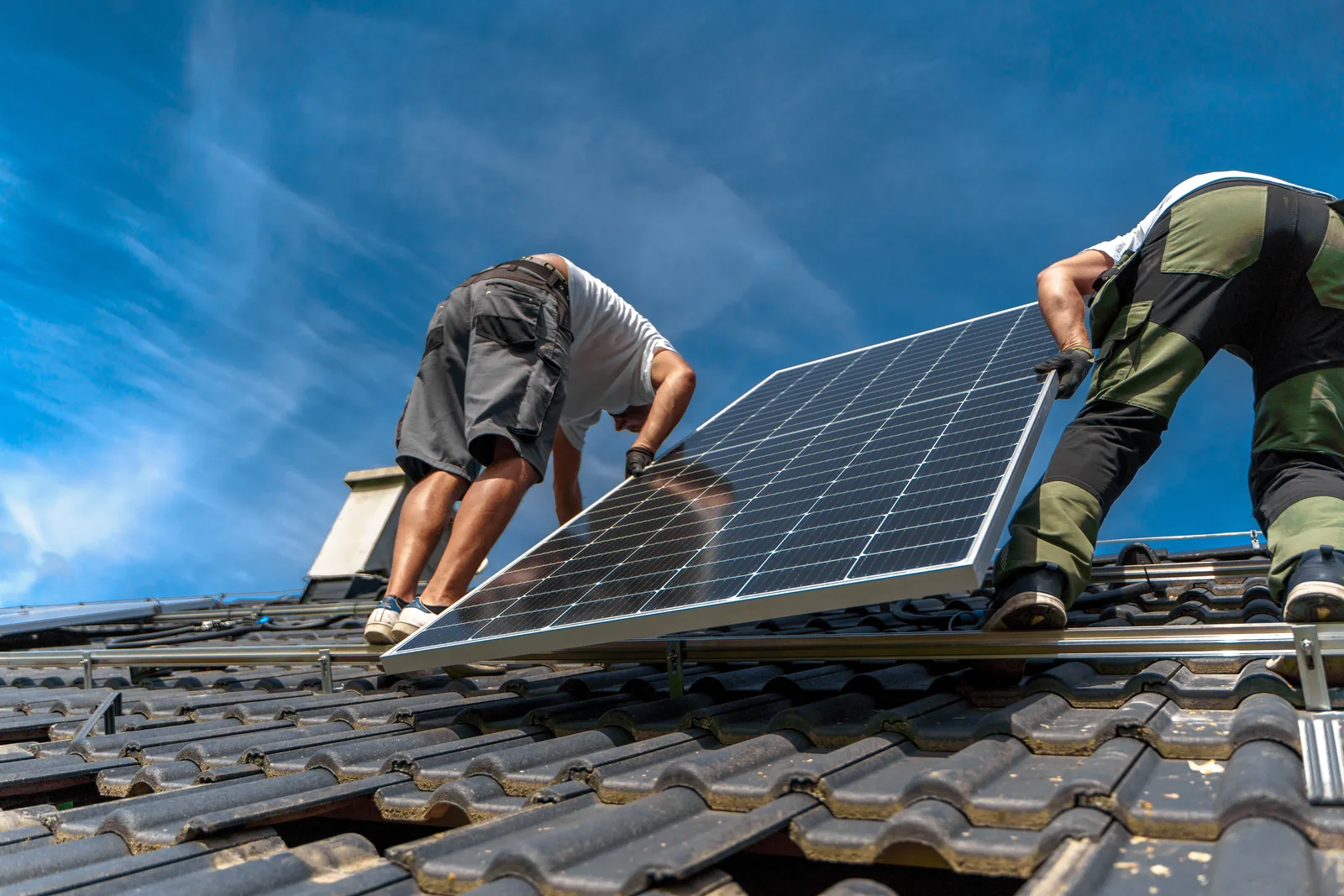 Zwei Monteure setzen auf einem Ziegeldach ein Solarmodul in die Unterkonstruktion ein