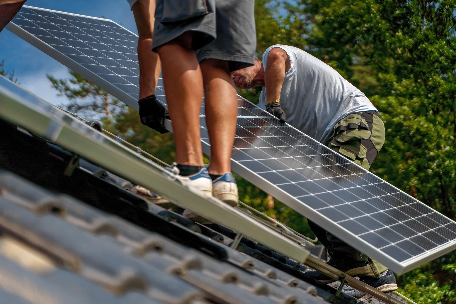 Zwei Monteure setzen auf einem Ziegeldach gemeinsam ein Solarmodul in die Schiene